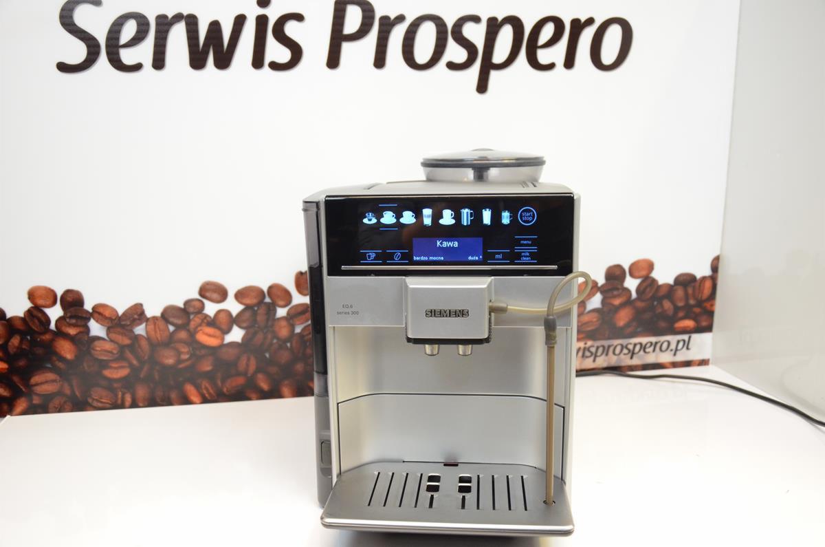 Automatyczny ekspres do kawy Siemens EQ.6 series 300 na tle reklamy Serwis Prospero z motywem ziaren kawy.