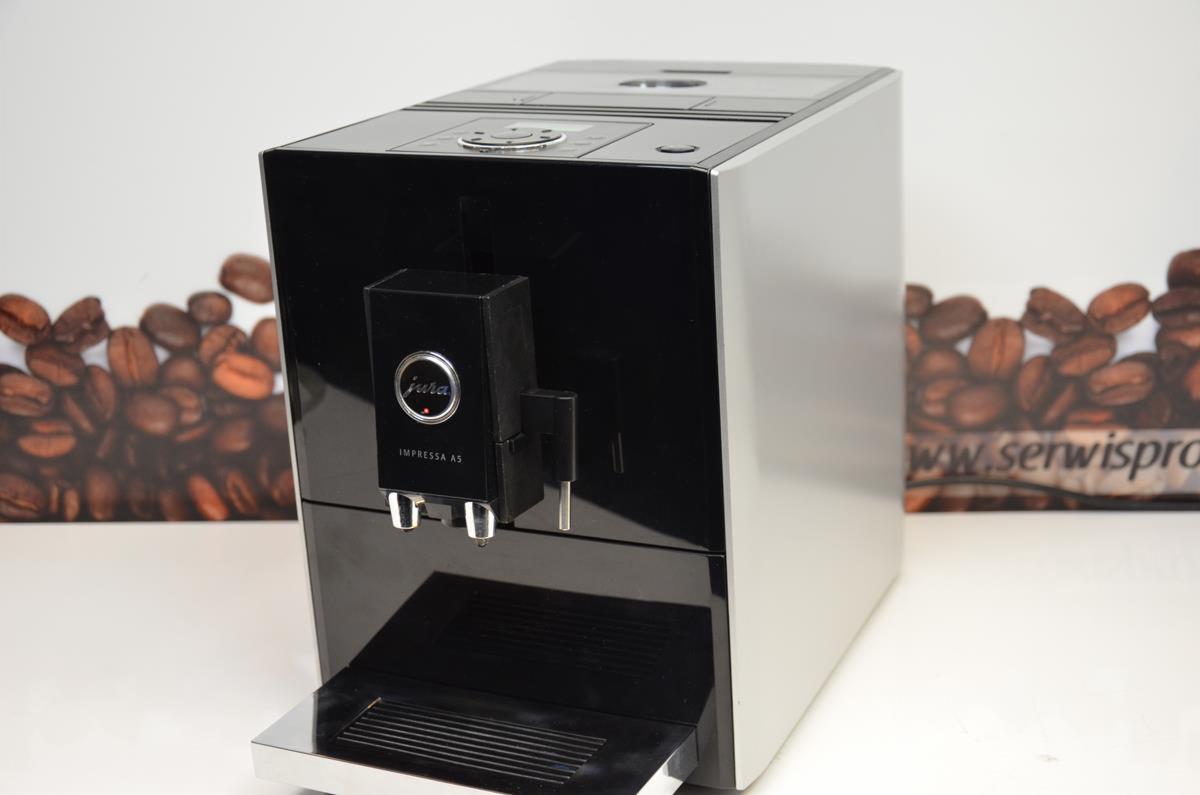 Automatyczny ekspres do kawy Jura Impressa A5 w kolorze czarno-srebrnym, z widocznym logo i dyszą, na białym tle z kartą z ziarnami kawy w tle.