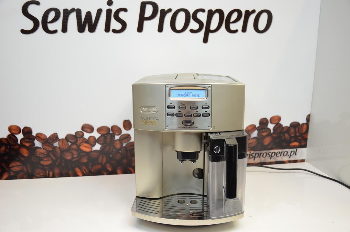 Automatyczny ekspres do kawy DeLonghi Magnifica, z wyświetlaczem LCD wskazującym 'Ready Standard Taste', na tle grafiki z ziarnami kawy i napisem 'Serwis Prospero' oraz adresem strony internetowej.