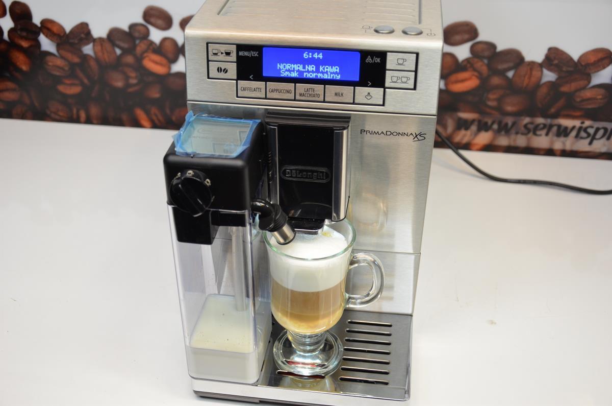 Automatyczny ekspres do kawy DeLonghi Primadonna XS przygotowuje latte macchiato w szklanej filiżance, wyświetlacz LCD pokazuje tryb 'Normalna Kawa'.