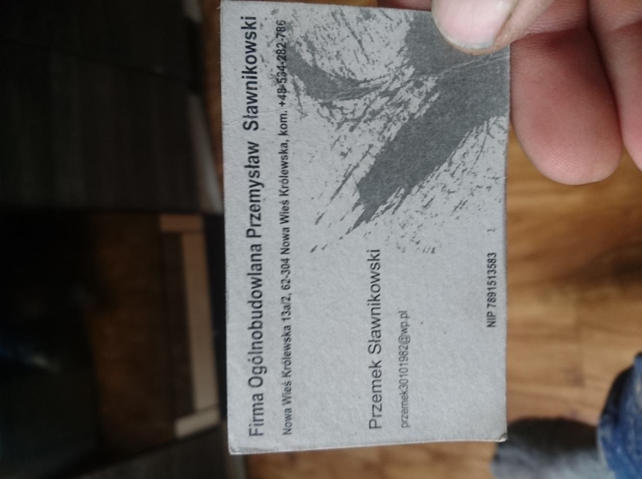 Wizytówka firmy ogólnobudowlanej Przemysława Sławnikowskiego, z adresem, numerem telefonu i adresem e-mail, trzymana w palcach.