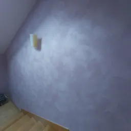 Ściana w odcieniach fioletu z dekoracyjną strukturą, oświetlona lampą ścienną, widoczne schody drewniane.