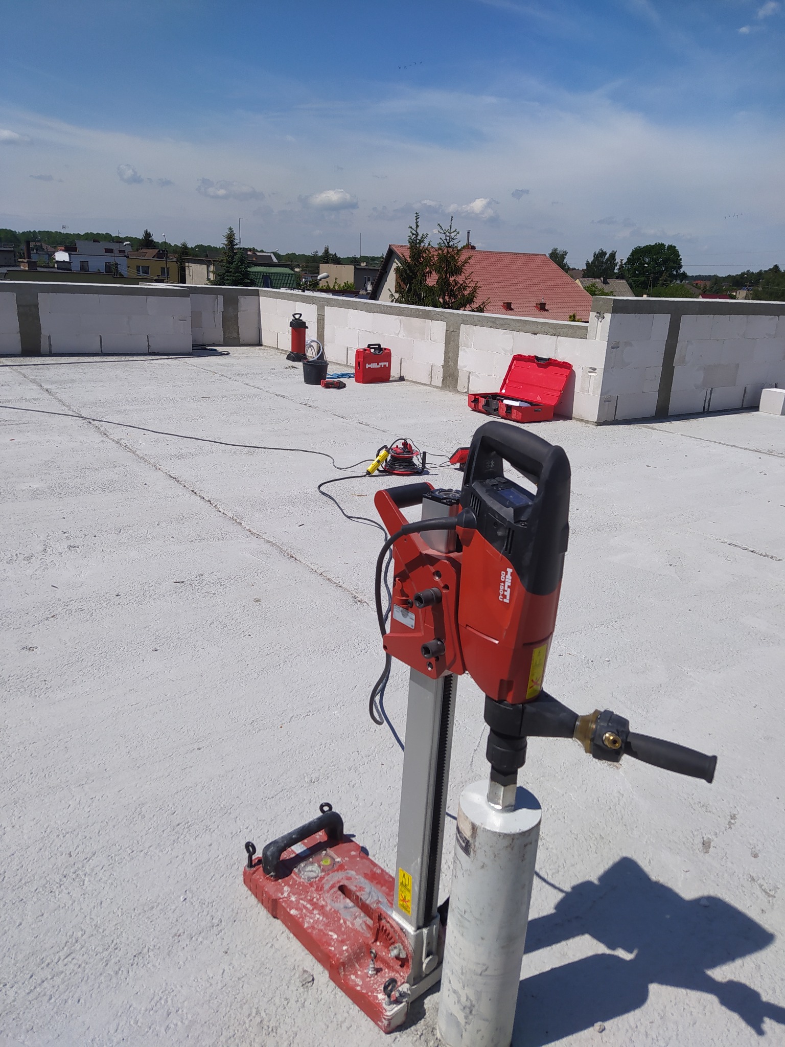 Wiertnica diamentowa Hilti DD 150-U na statywie, przygotowana do wiercenia otworów w betonowym stropie budynku w stanie surowym otwartym, z widocznymi akcesoriami i skrzynką narzędziową w tle.