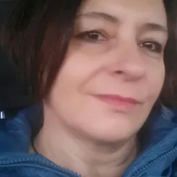 Portret kobiety w niebieskiej kurtce, z delikatnym uśmiechem, skierowana delikatnie w lewo.