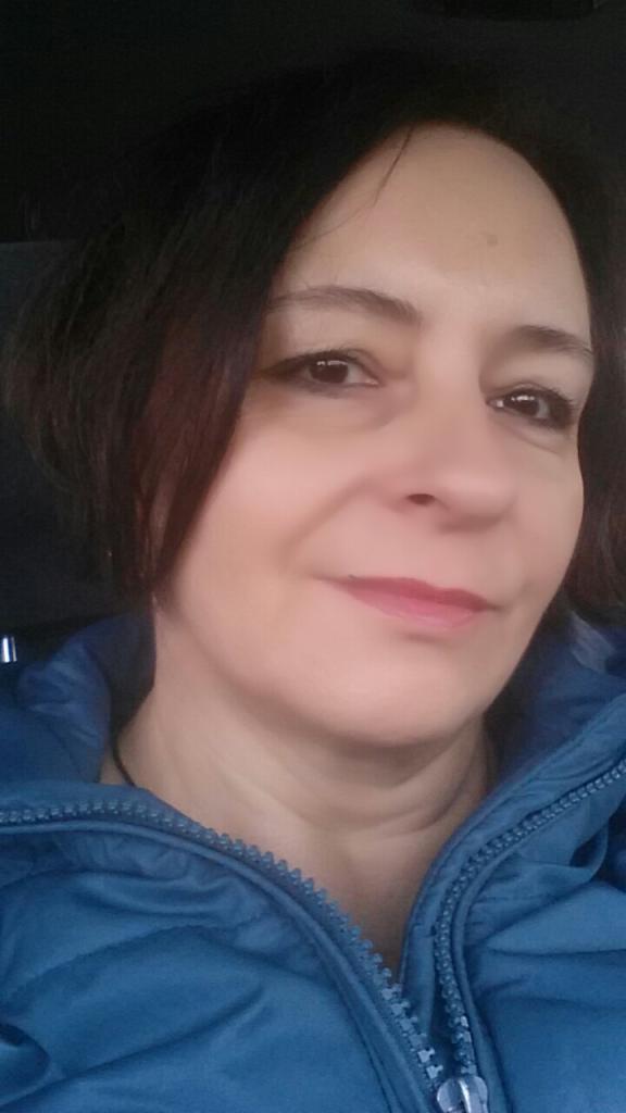 Portret kobiety w niebieskiej kurtce, z delikatnym uśmiechem, skierowana delikatnie w lewo.