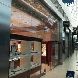 Wnętrze galerii handlowej z widoczną witryną sklepu jubilerskiego A&A po umyciu, z boku stoi niebieski wózek z napisem 'Caution Wet Floor', logo firmy sprzątającej Fabryka Czystości w górnym rogu.