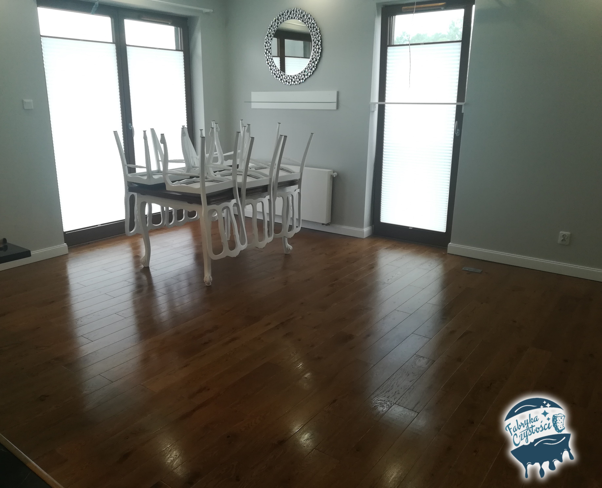 Wypolerowana podłoga z parkietu w pustym pokoju z odwróconymi krzesłami na stole, przygotowana do sprzątania.