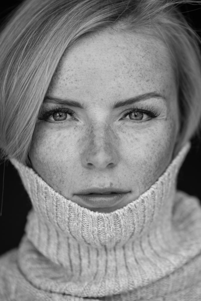 Portret kobiety z piegami, w swetrze z golfem, czarno-biały, z delikatnym uśmiechem.