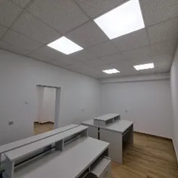 Wnętrze biura po malowaniu w Łodzi: białe ściany, podwieszany sufit z oświetleniem, jasne biurka, drewnopodobna podłoga. Widok na odnowione pomieszczenie.