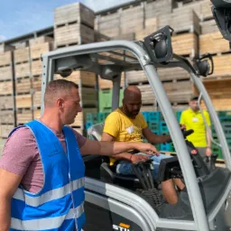 Instruktor w niebieskiej kamizelce z napisem 'Ausbilder Rafał Markowski' nadzoruje pracę operatora wózka widłowego Still, w tle stos palet.