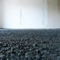 Szara, mokra wylewka na podłodze w trakcie wykonywania, widoczny pracownik zacierający powierzchnię w jasnym pomieszczeniu z surowymi ścianami.