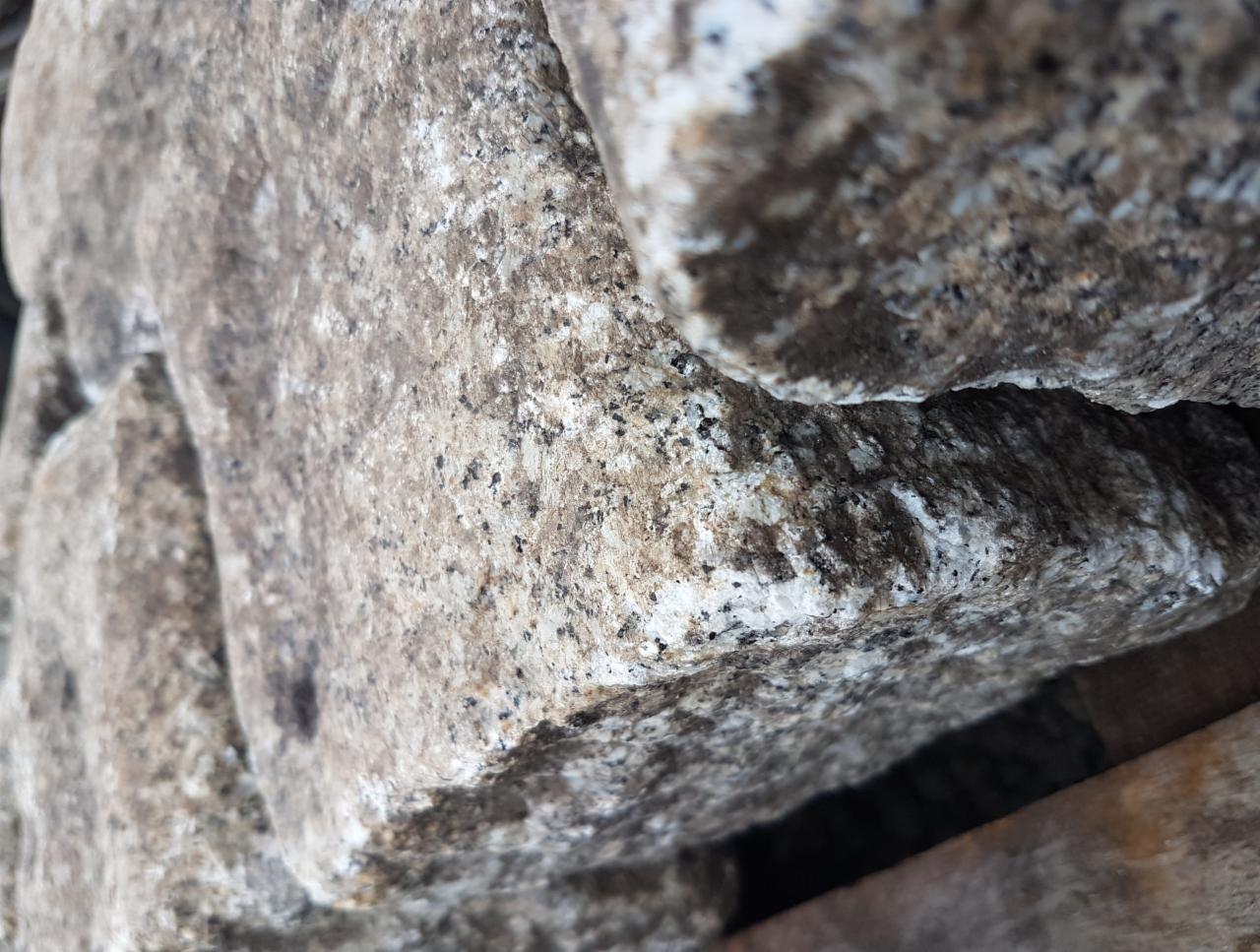 Bliski kadr na ułożone, szare kamienie granitowe o zróżnicowanej fakturze, z widocznymi ciemnymi i jasnymi plamkami, oświetlone naturalnym światłem.