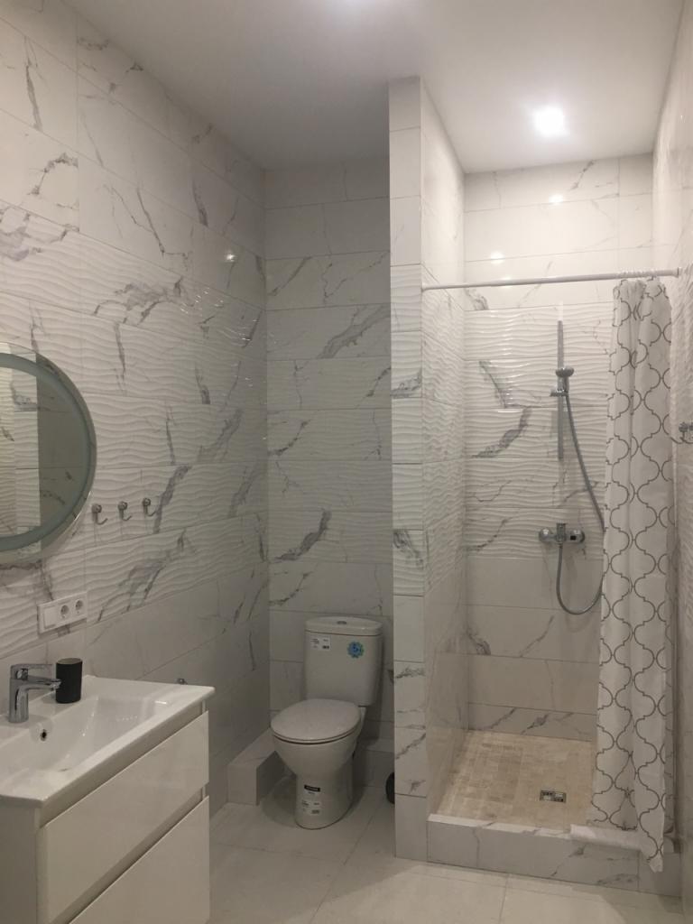 Biała łazienka z umywalką, toaletą i prysznicem wykończona płytkami imitującymi marmur, z dekoracyjną falistą fakturą na ścianach.