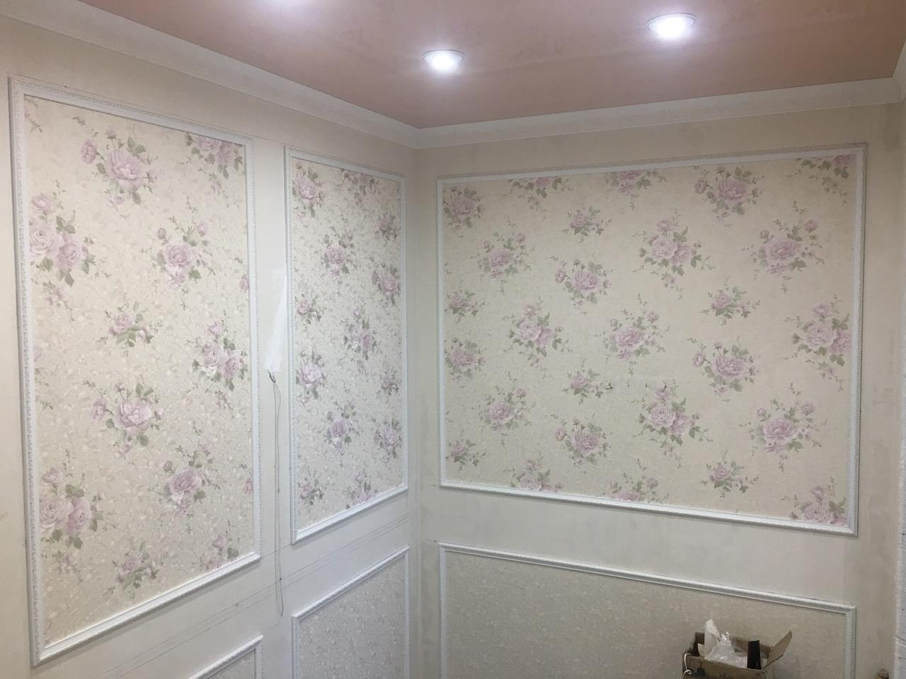 Ściany z dekoracyjnymi panelami i tapetą w kwiaty, wykończone białą listwą przysufitową i podłogową, sufit w odcieniu pudrowego różu, widoczny fragment kartonu w rogu.