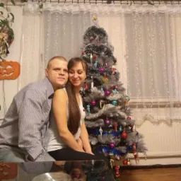 Para siedzi na tle choinki z ozdobami i białych firanek, dekoracja dyni na ścianie, odbicie w blacie stołu.