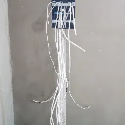 Wewnętrzna puszka instalacyjna z wystającymi przewodami elektrycznymi w trakcie montażu, widoczne rury instalacyjne w podłodze, surowy stan wykończenia ścian.