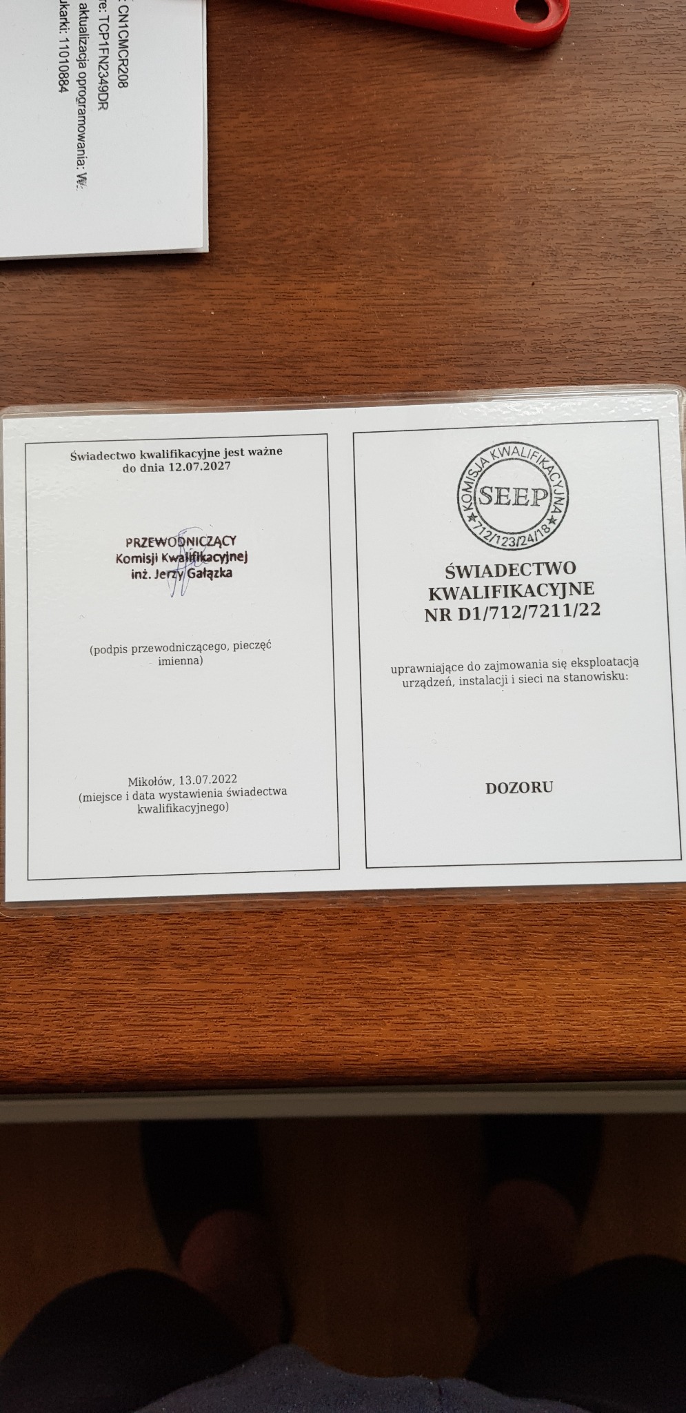 Świadectwo kwalifikacyjne SEEP z datą ważności do 12.07.2027, uprawniające do eksploatacji urządzeń, instalacji i sieci na stanowisku dozoru. Dokument na drewnianym tle.