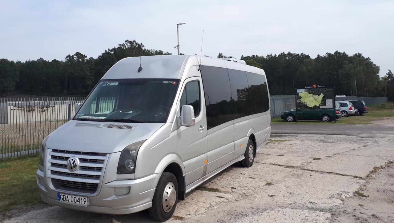 Srebrny bus Volkswagen Crafter z przyciemnianymi szybami na parkingu, widoczny znak Gmina Bełżec w tle.
