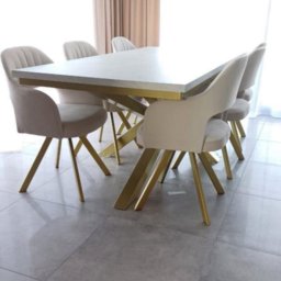 Meble Damian Góralski - Jasny stół z blatem imitującym kamień i złotymi nogami w kształcie litery X, otoczony krzesłami z beżową tapicerką i złotymi nogami, pod nowoczesną lampą.