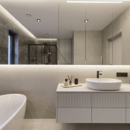 Meble Damian Góralski - Nowoczesna łazienka z umywalką nablatową, szafką z frezowanymi frontami i dużym lustrem z podświetleniem LED. Widoczna wanna i kabina prysznicowa w tle.