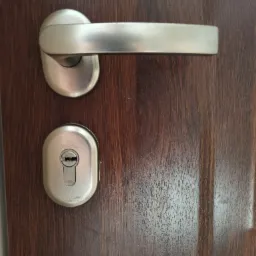 Szczegółowe ujęcie klamki i zamka w drzwiach z ciemnego drewna, widoczne ślady użytkowania.