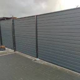 Nowoczesna, przesuwna brama wjazdowa z poziomych paneli w kolorze grafitowym, z widocznymi elementami mocującymi i odpływem liniowym w kostce brukowej.