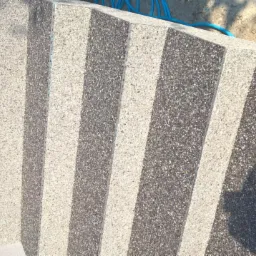 Balkon z wykończeniem z mozaiki kamiennej w odcieniach szarości i bieli, widoczne fragmenty niebieskiego węża ogrodowego na górze