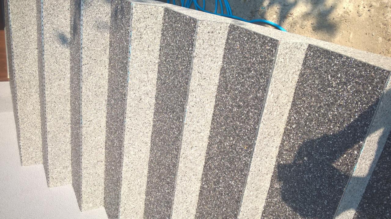 Balkon z wykończeniem z mozaiki kamiennej w odcieniach szarości i bieli, widoczne fragmenty niebieskiego węża ogrodowego na górze