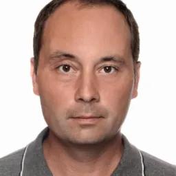 Portret mężczyzny w szarej koszulce polo na białym tle. Ujęcie en face, neutralny wyraz twarzy, oświetlenie studyjne.