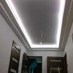 Nowoczesny sufit podwieszany z oświetleniem LED w kształcie prostokąta, widok z dołu na trzy brązowe drzwi z przeszkleniami i drewnianą drabinę opartą o ścianę.