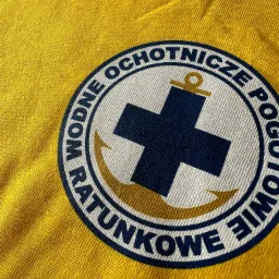 Żółta koszulka z nadrukowanym okrągłym logo Wodne Ochotnicze Pogotowie Ratunkowe z krzyżem i kotwicą.