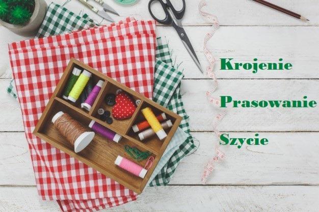 Przybornik krawiecki z nićmi, guzikami i serduszkiem na tle czerwono-białej i zielono-białej kraty, obok leżą nożyczki, centymetr krawiecki i ołówek na białym drewnianym stole.