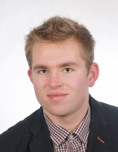 Portret młodego mężczyzny w koszuli w kratę i marynarce na białym tle. Uśmiechnięty, z krótkimi blond włosami, patrzy wprost w obiektyw.