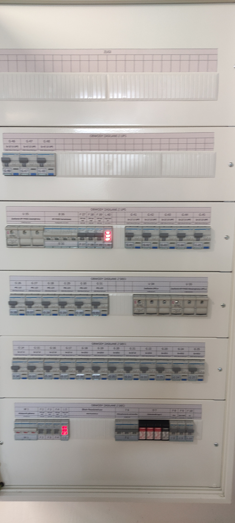 Rozdzielnica elektryczna z bezpiecznikami i opisami obwodów, widok z bliska, oświetlenie górne, detale instalacji.