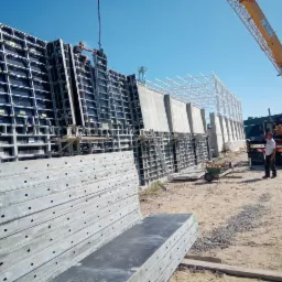 Montaż szalunków na budowie hali z elementami żelbetowymi, widoczny dźwig i pracownicy, w tle konstrukcja stalowa dachu.