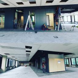 Grupa Magmat Magdalena Matysiak - Prace wykończeniowe w biurze: montaż ścianek działowych i prace malarskie, widoczne drabiny, narzędzia i ekipa remontowa w trakcie pracy.