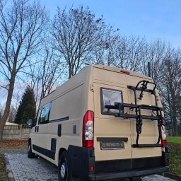 Uretanowe M Sp. z o. o. - Beżowy kamper z bagażnikiem rowerowym, pokryty natryskową powłoką poliuretanową, widoczny na zewnątrz w pochmurny dzień. Teksturowana powierzchnia.