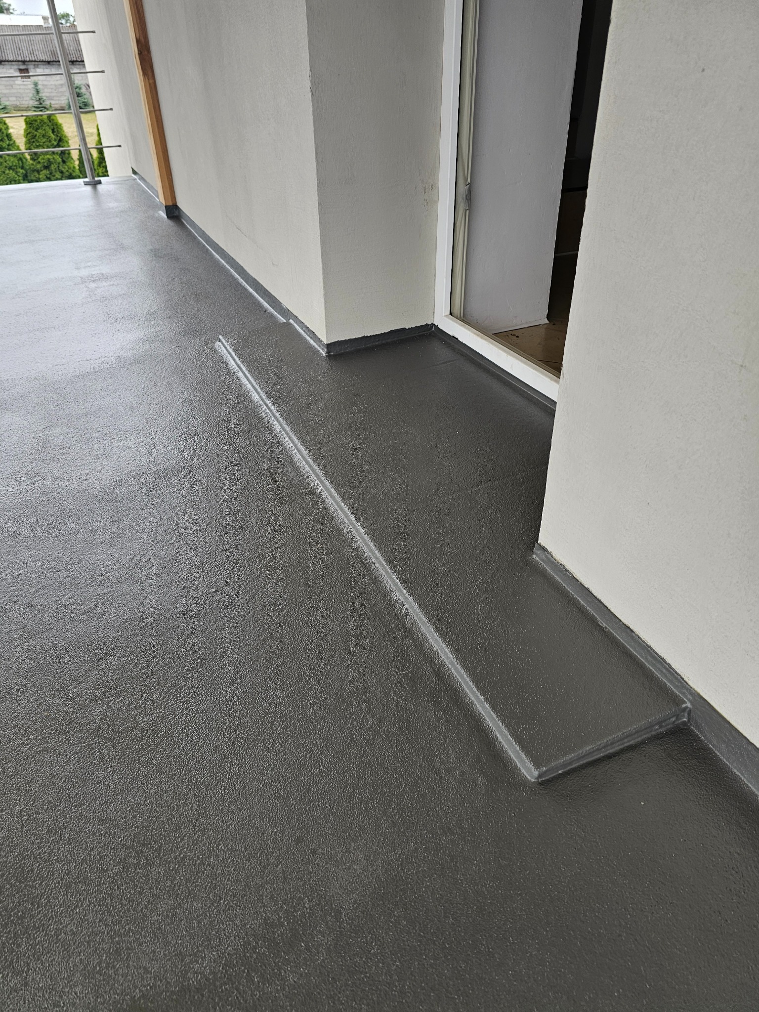 Szara, gładka posadzka żywiczna na balkonie z pojedynczym stopniem i widocznym wejściem do budynku. Realizacja z dbałością o detale wykończeniowe.