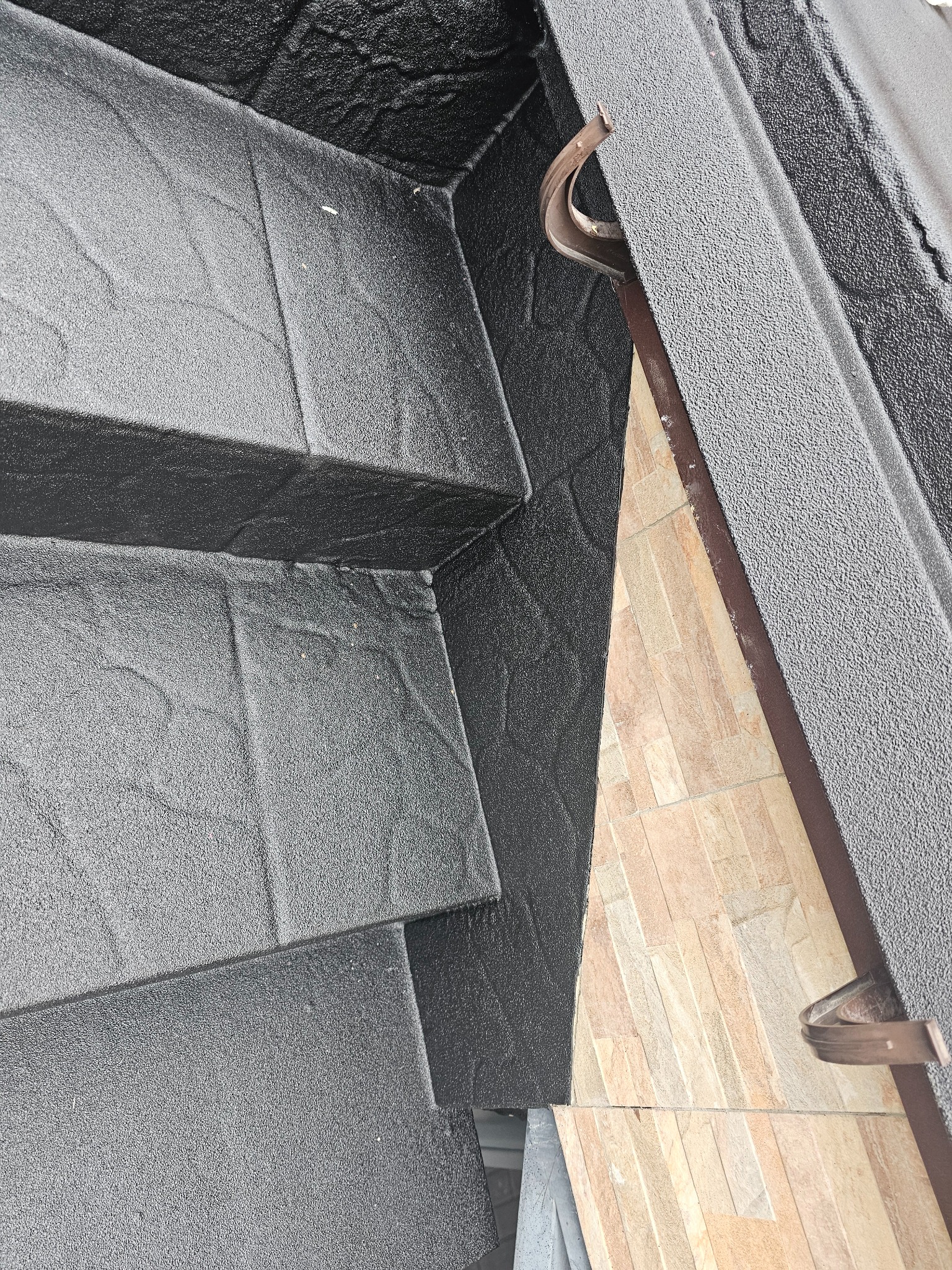 Czarna, szorstka posadzka żywiczna schodów zewnętrznych, z widocznym fragmentem elewacji w ciepłych odcieniach i rynną. Tekstura i detale wykończenia.