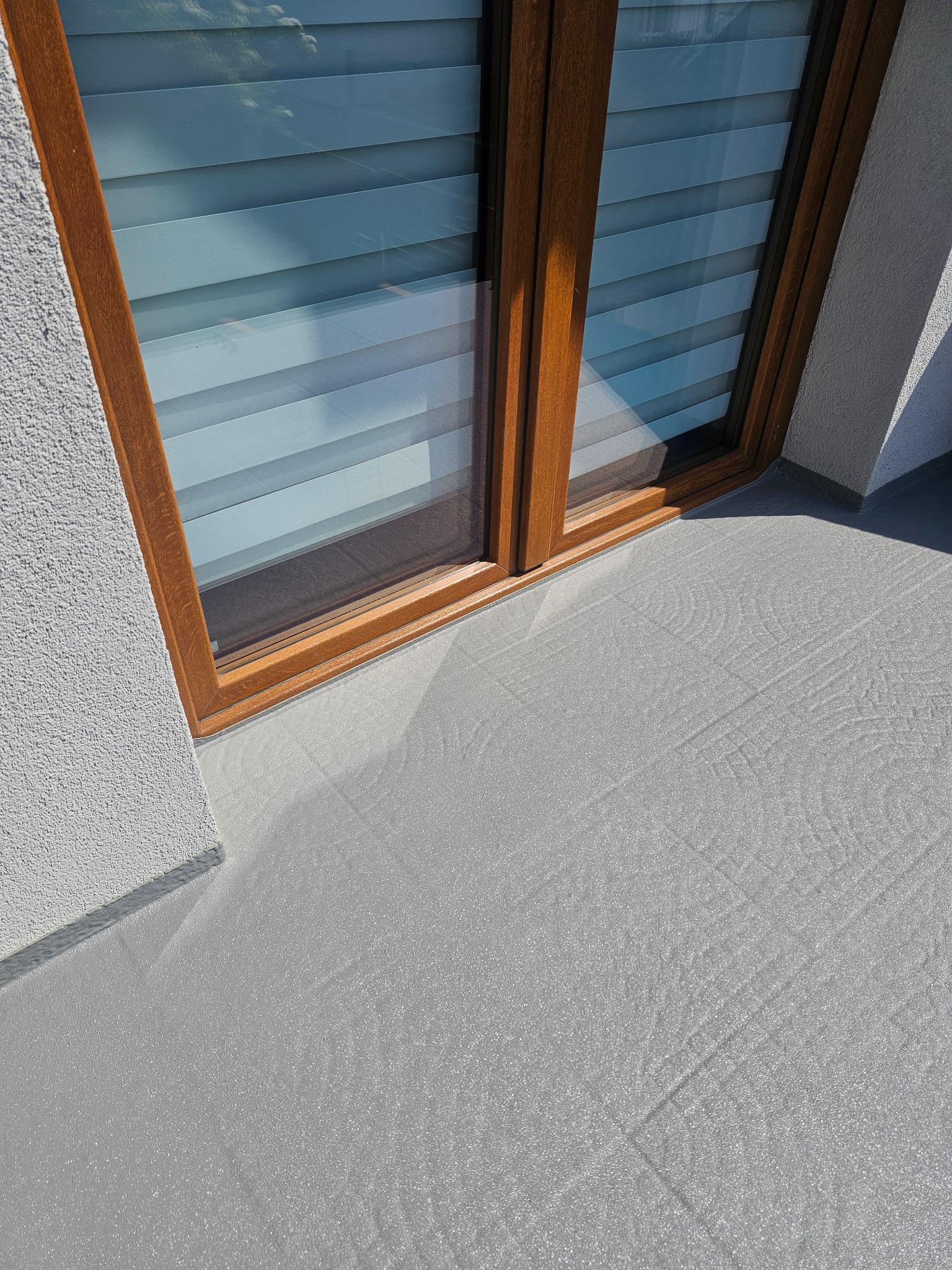 Szara, wzorzysta posadzka żywiczna na balkonie, widok z góry, drewniana rama okienna. Nowoczesne wykończenie balkonu z bliska.