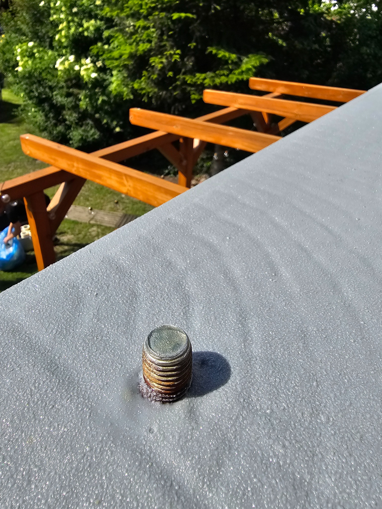 Szara, chropowata powierzchnia z metalowym elementem mocującym na tle drewnianej konstrukcji i zieleni. Detal ocieplenia pianką PUR z bliska.