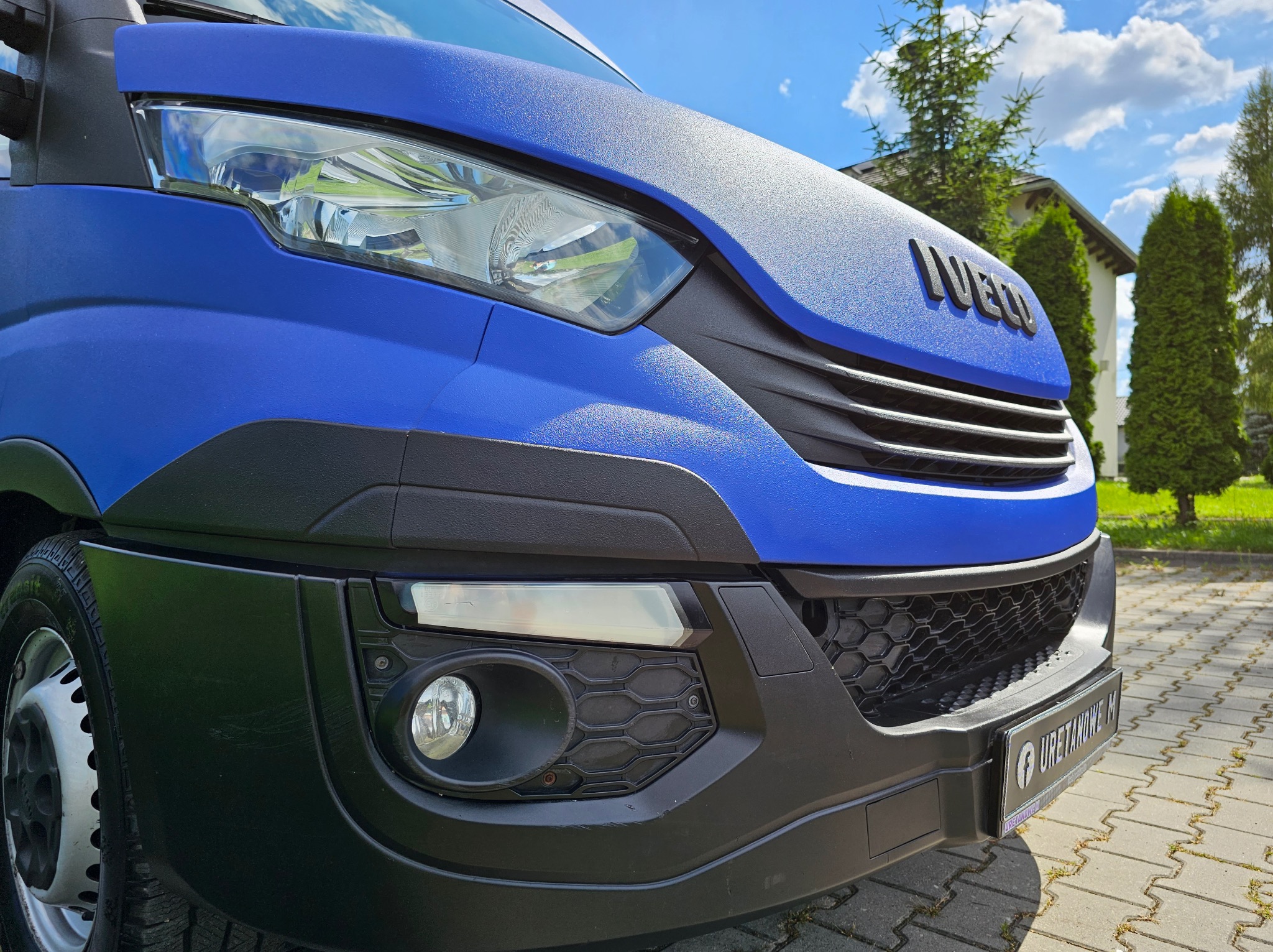 Niebieski samochód dostawczy Iveco z fakturą na karoserii, prawdopodobnie po aplikacji ochronnej powłoki. Widoczne logo firmy na tablicy rejestracyjnej.
