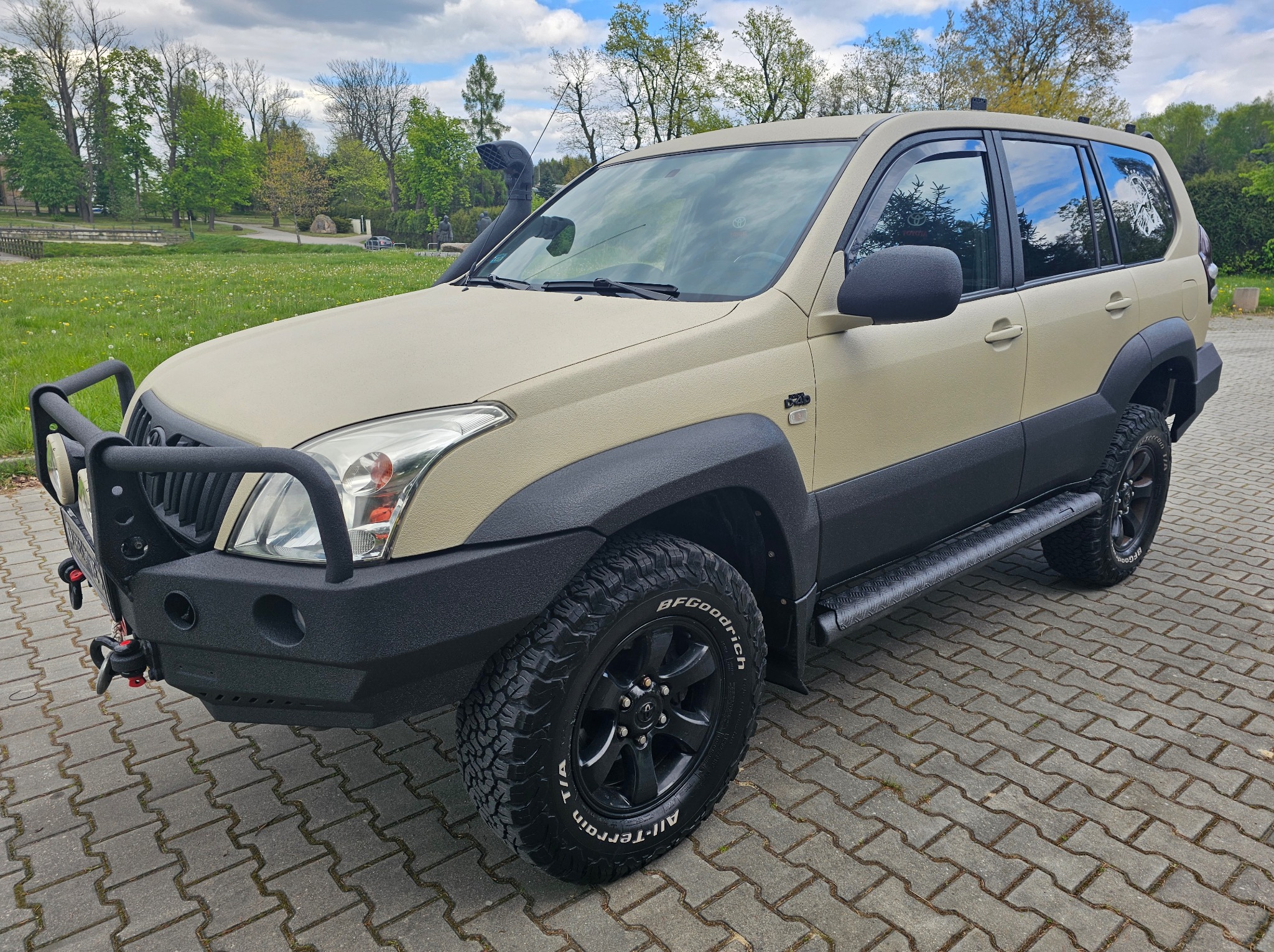 Toyota Land Cruiser po aplikacji beżowej powłoki ochronnej z fakturą, z czarnymi elementami off-road, na tle zieleni.