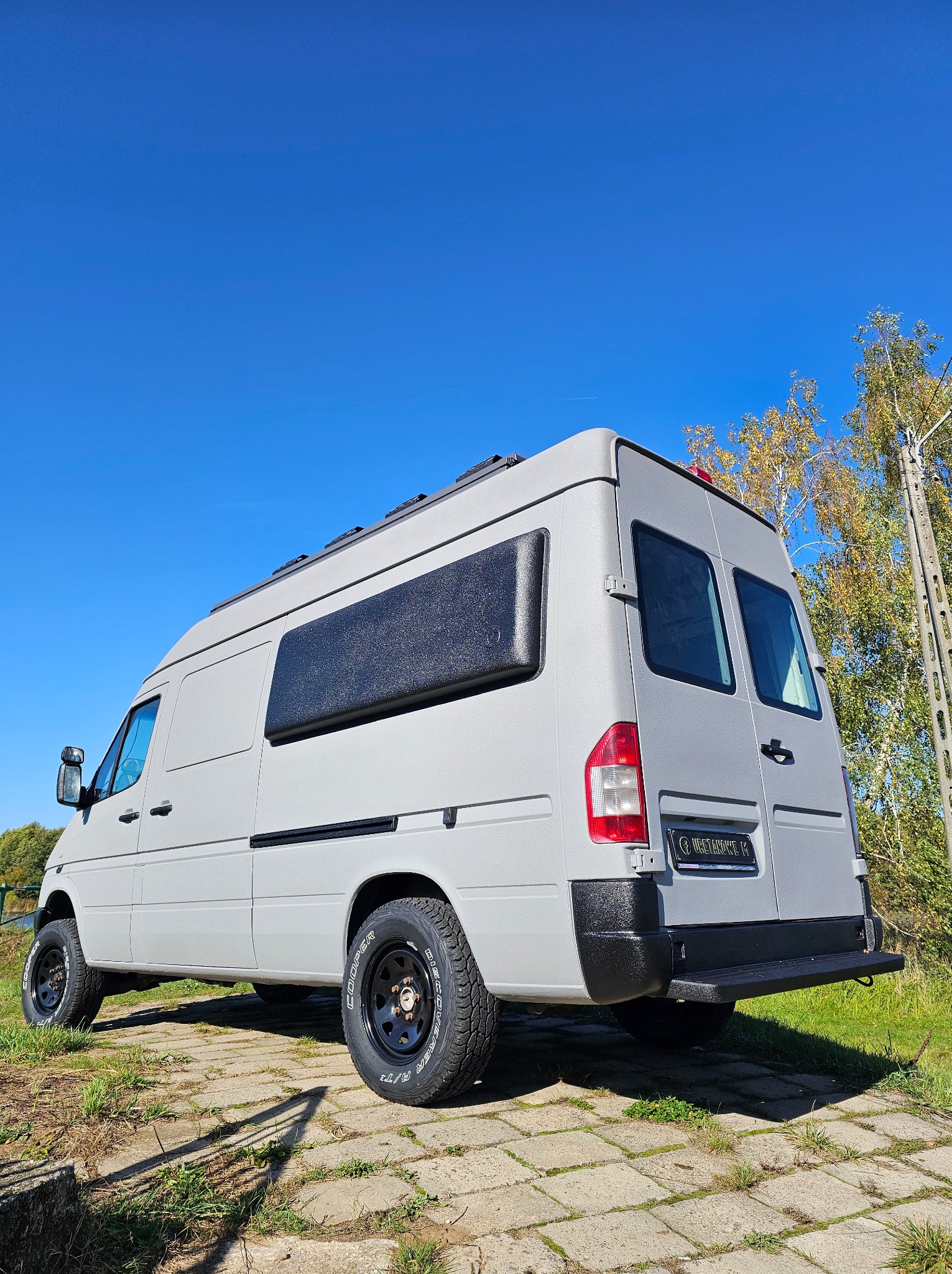 Szary van po aplikacji ochronnej powłoki, widoczna faktura i czarne akcenty. Ujęcie z dołu podkreśla terenowy charakter pojazdu na tle błękitnego nieba.