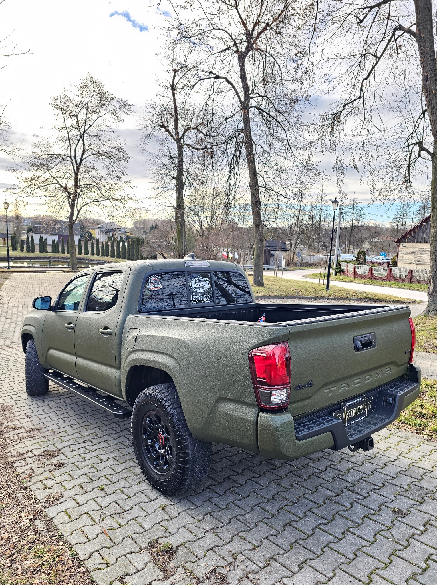 Toyota Tacoma po aplikacji ochronnej powłoki w kolorze khaki, widoczna faktura. Auto na kostce brukowej, w tle drzewa i zabudowania.