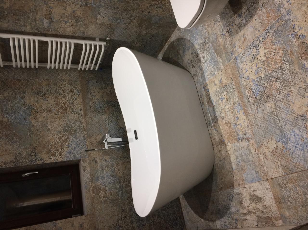 Nowoczesna, wolnostojąca wanna w łazience wykończonej płytkami w stylu vintage, z grzejnikiem drabinkowym i ciemnym oknem w tle.