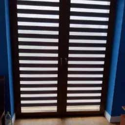 Dwuskrzydłowe okno z zamontowanymi roletami w poziome pasy, widok z wnętrza pokoju z niebieskimi ścianami.