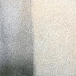 Fragment ściany z widocznym zabrudzeniem, prawdopodobnie po myciu ciśnieniowym, ukazujący różnicę w kolorze i strukturze powierzchni przed i po czyszczeniu.