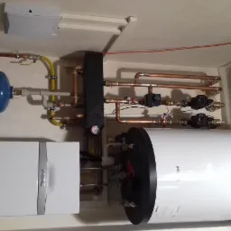 Kotłownia z piecem gazowym Vaillant, zasobnikiem ciepłej wody, naczyniem przeponowym i instalacją z rur miedzianych w pomieszczeniu o beżowych ścianach.