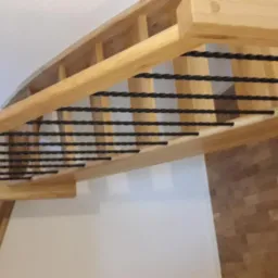 Drewniana antresola z czarnymi, skręconymi metalowymi prętami, widok z dołu, naturalne oświetlenie.